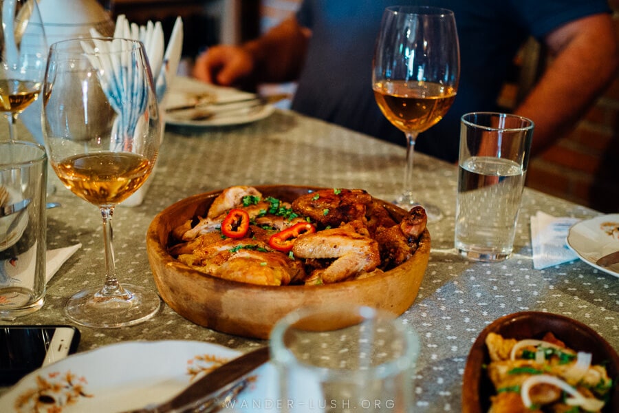 A wooden plate heaped with chicken and surrounded by glasses of amber-coloured wine.