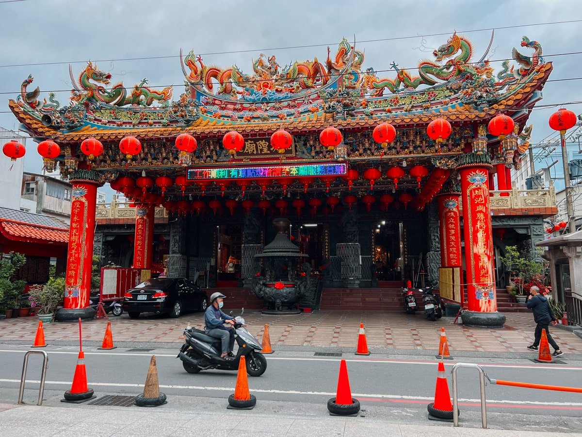 Taiwanese local driving on scooter past decorated red shrine on the street of Hualien City, Taiwan.