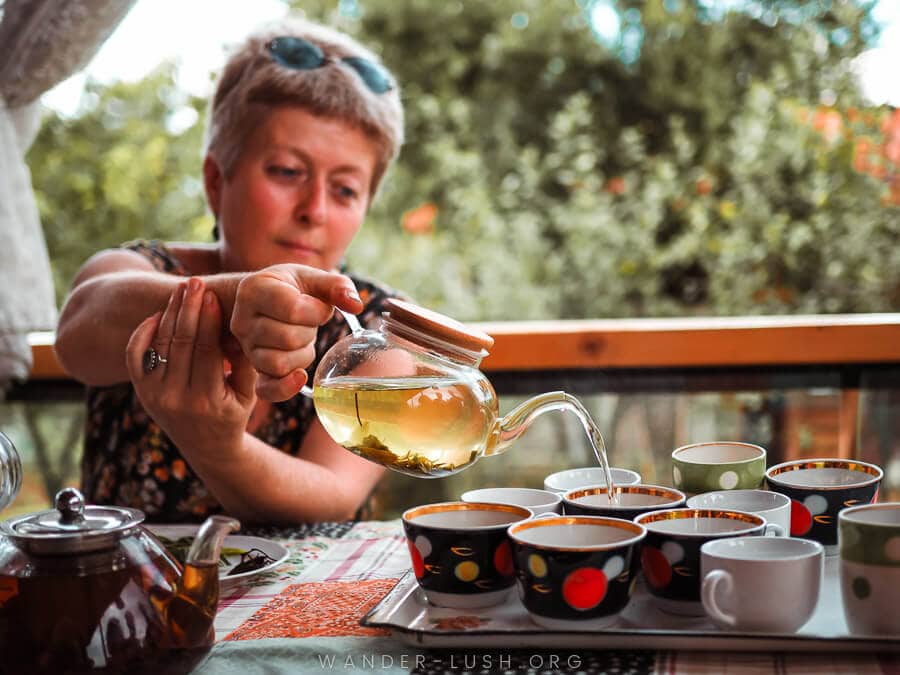 A woman pours tea from a glass pot into cups.