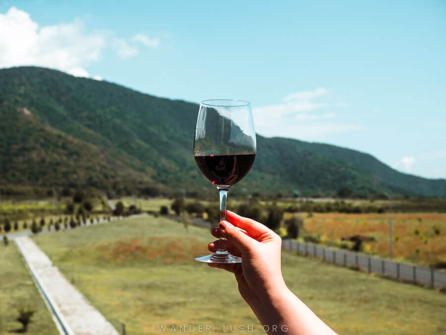 A woman holds a glass of wine in front of a mountain in Kakheti, Georgia.