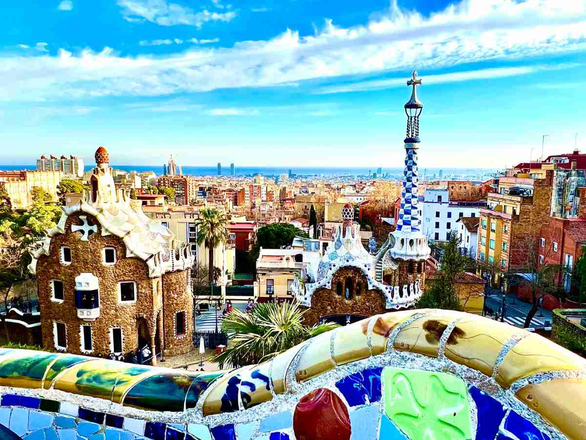 a colouful image of Park Güell Barcelona with the city's skyline. Blue skies with cotton clouds above the pretty city at almost sunset