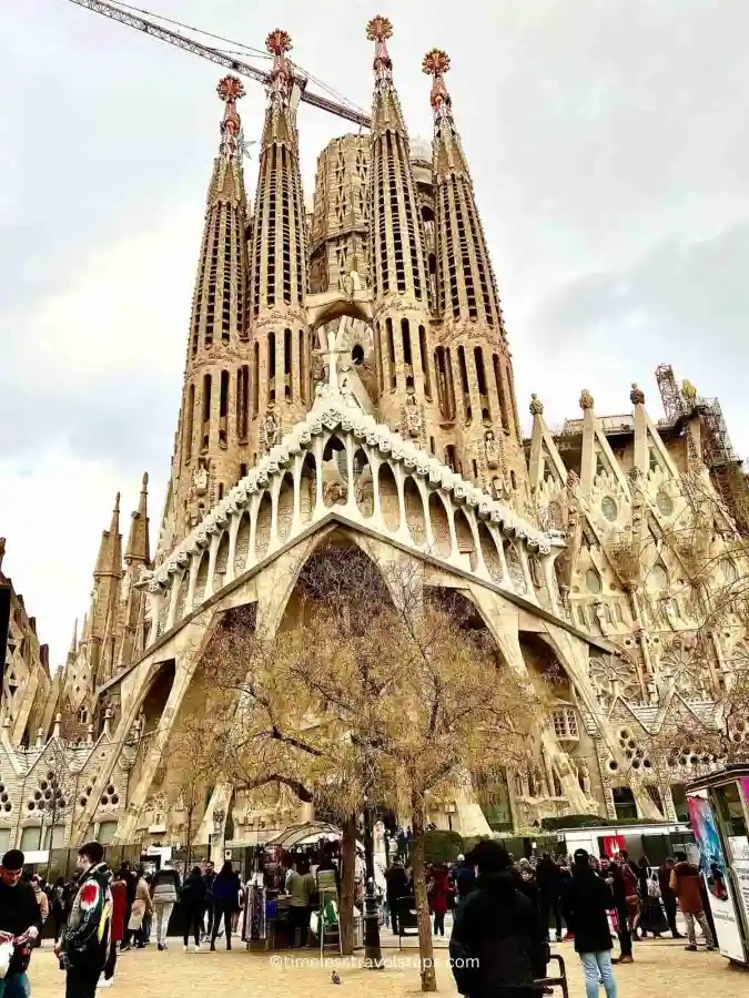 the frontal view of the Sagrada Familia. A huge creation. People in the foreground of the photo admiring and taking photos on a winter in Barcelona day