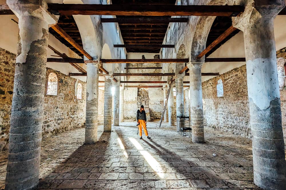 A woman in yellow pants standing inside an empty church in Voskopoja, Albania.