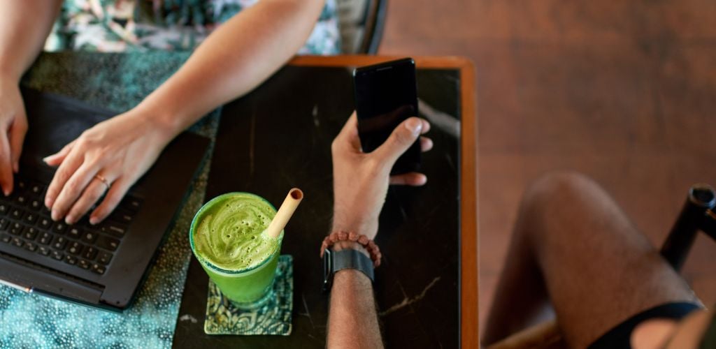 A couple coworkers surfing the web together on laptop and cellphone in trendy bohemian cafe