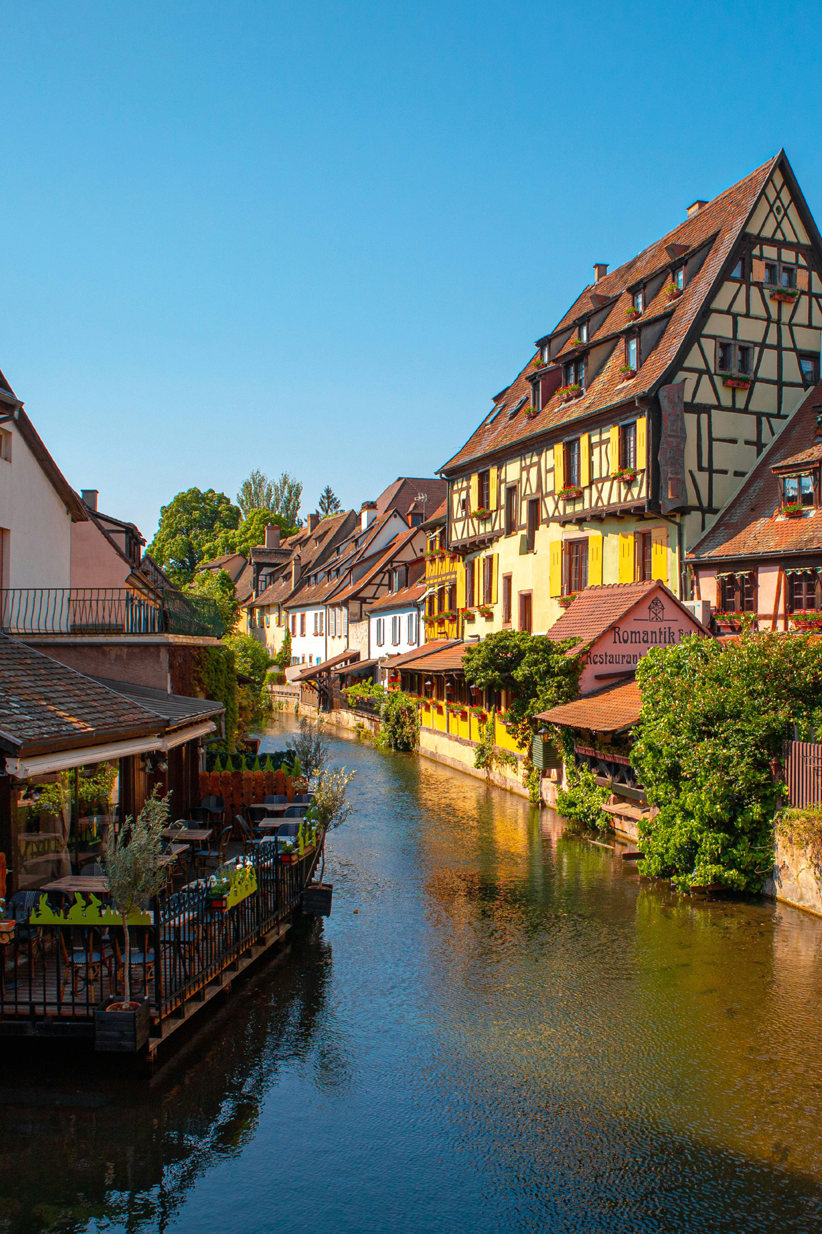 Half timbered homes in Strasbourg, France, along the banks of a river surrounded by restaurants and greenery.