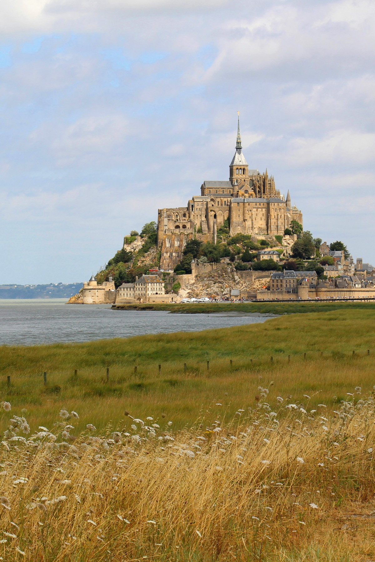 Mont-Saint-Michel rises in the distance above a streak of water and fields of green.