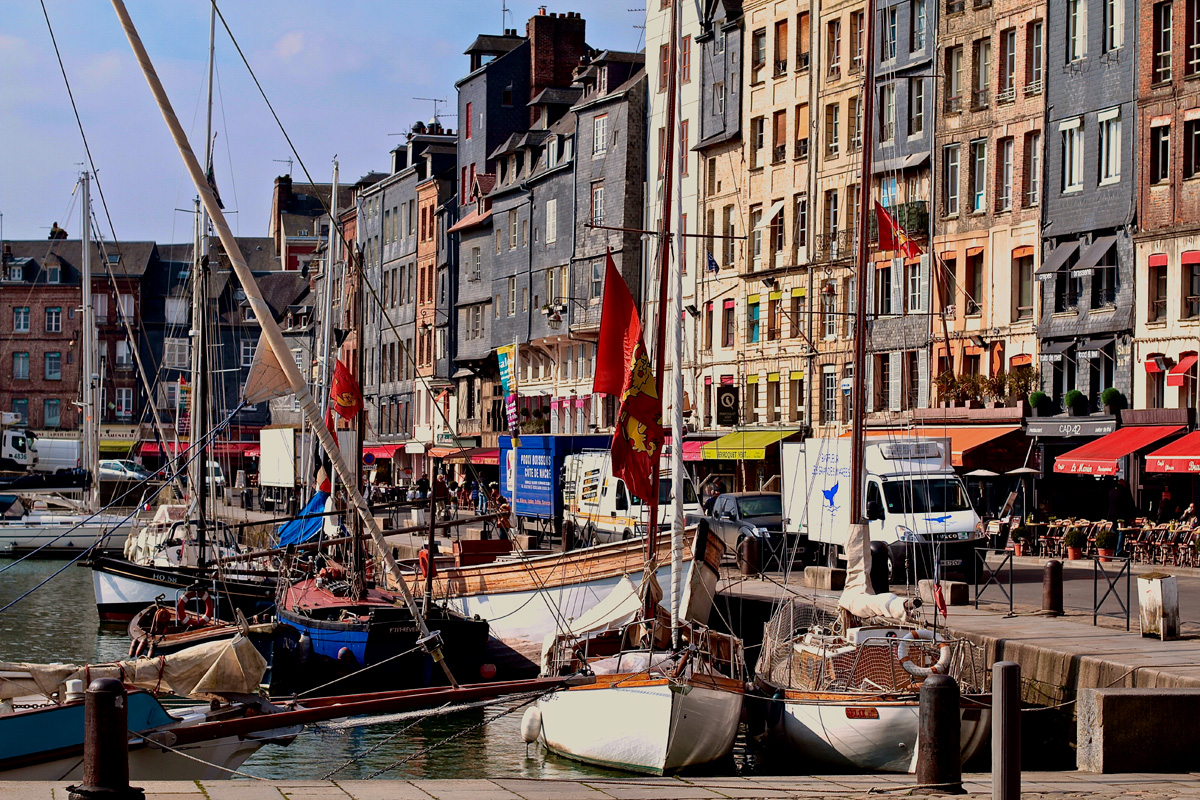 Lines of sail boats in front of a row of charming riverside buildings in Honfleur, France.