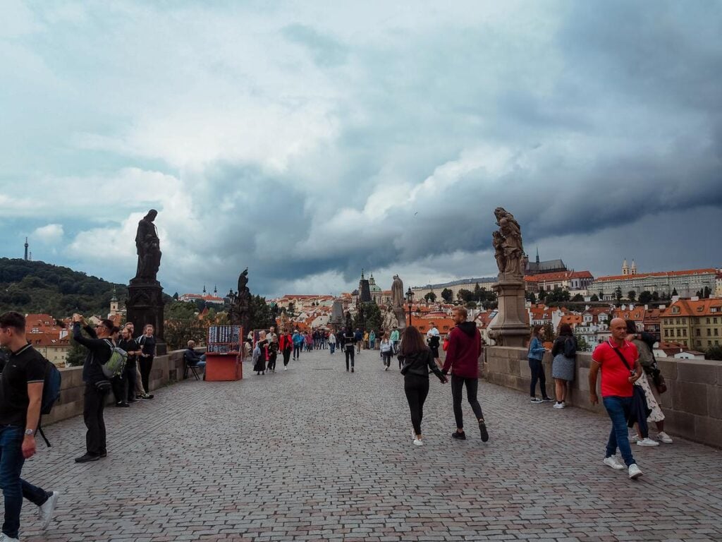 Tourists walking on Charles Bridge with Prague Castle in skyline.