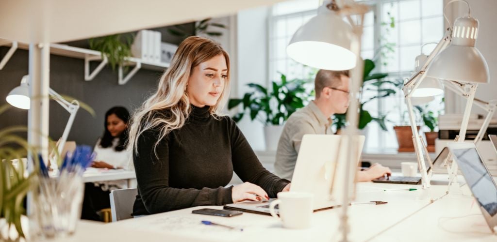 A woman wearing a black sweat shirt is busy working with her laptop in the coworking space. 