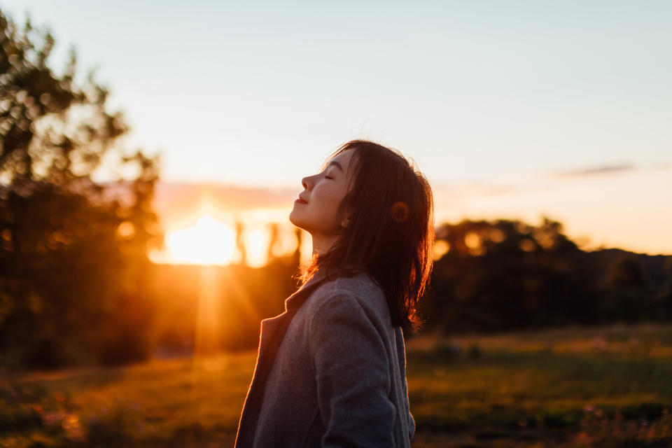 A woman standing at dusk, with her head back and eyes closed, looking content