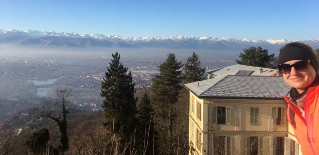 A woman photographs an aerial picture of Turin and a snowy peak in the distance. 
