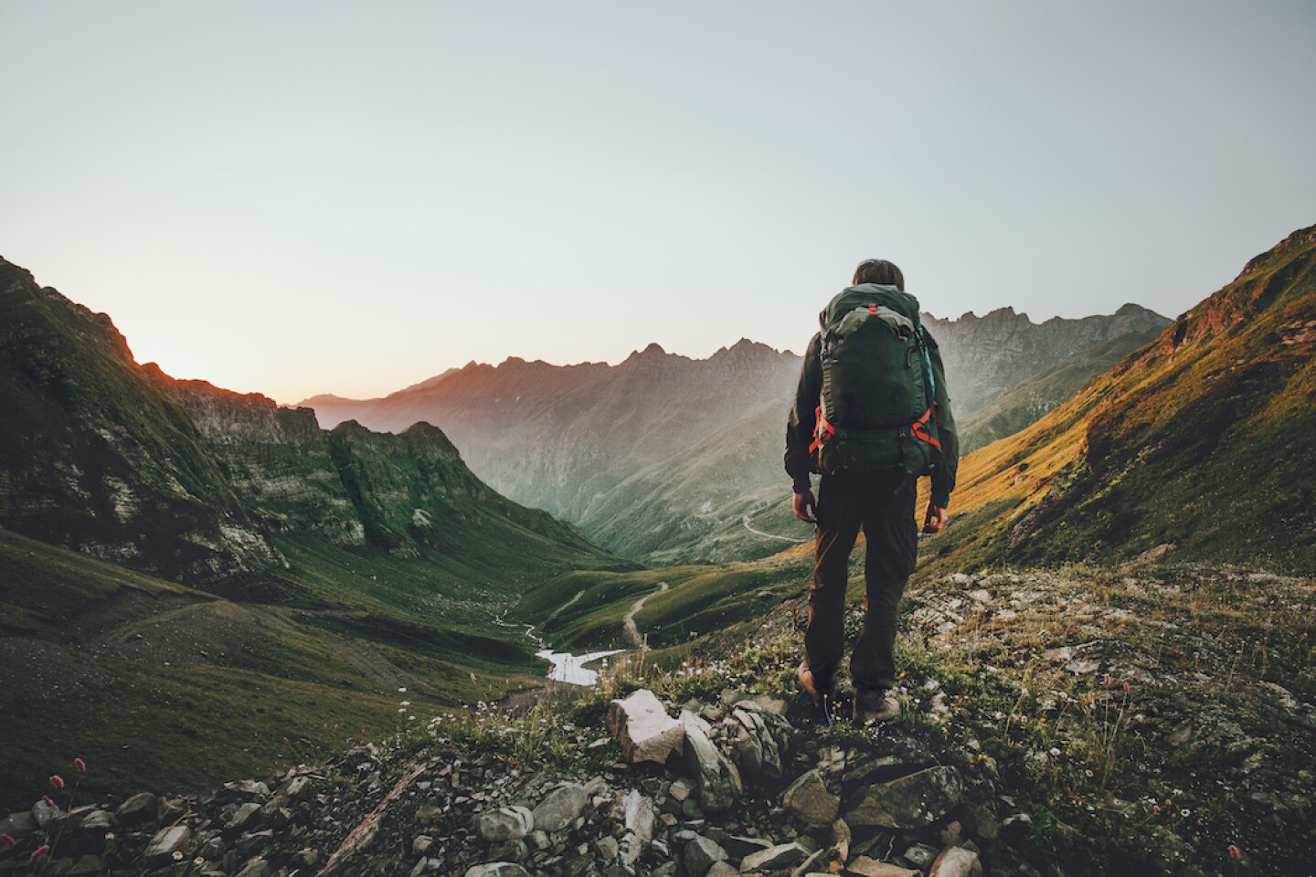 The back of a person wearing a backpack as they hike through a mountainous valley