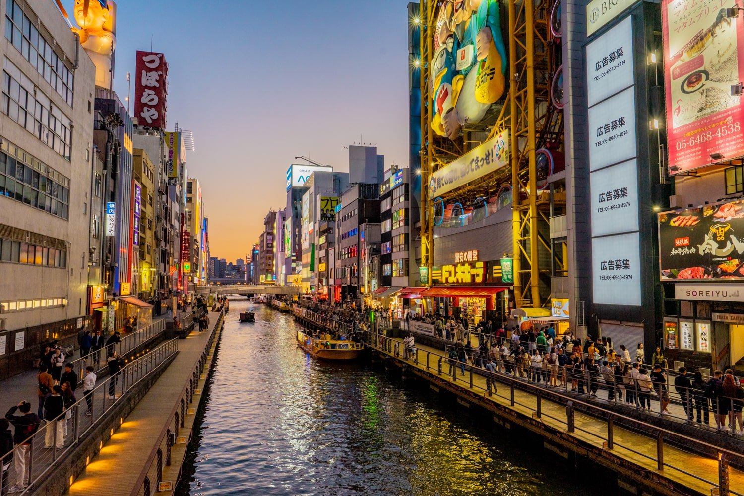 Neon lights and tourist crowding the streets lining the Dotonbori canal in Osaka, Japan.