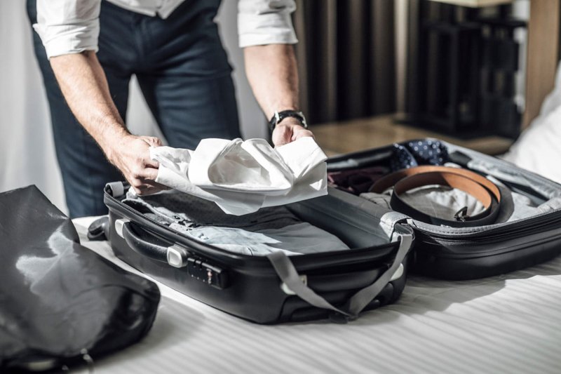 A person packing their suitcase with dress clothing.