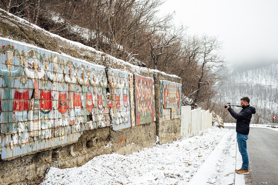 A long concrete wall on the roadside in Tianeti, Georgia covered with colourful ceramic mosaics.