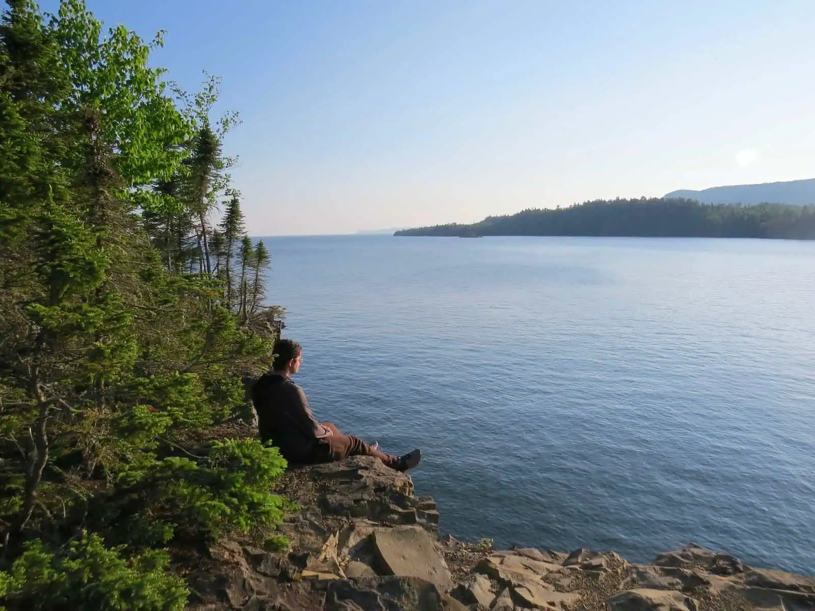 A man sitting on a rock with trees behind him overlooking Thunder Bay, Ontario, Canada