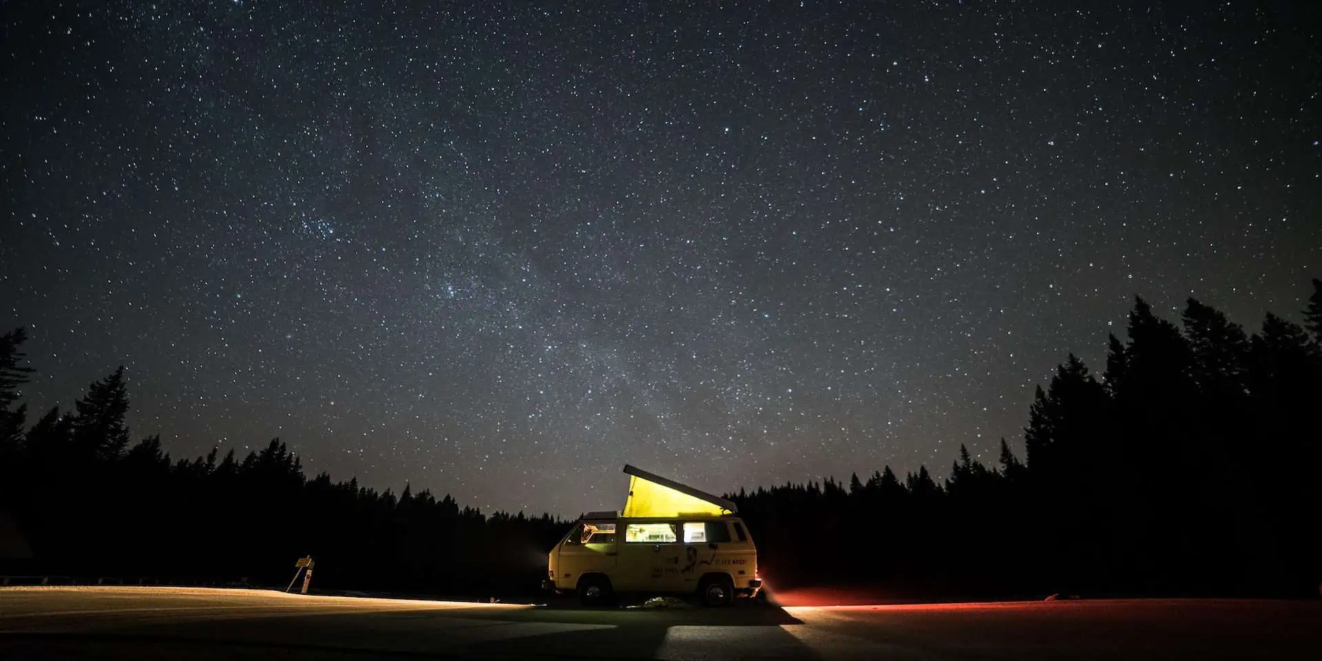 Road trip van parked at night with starry sky and trees