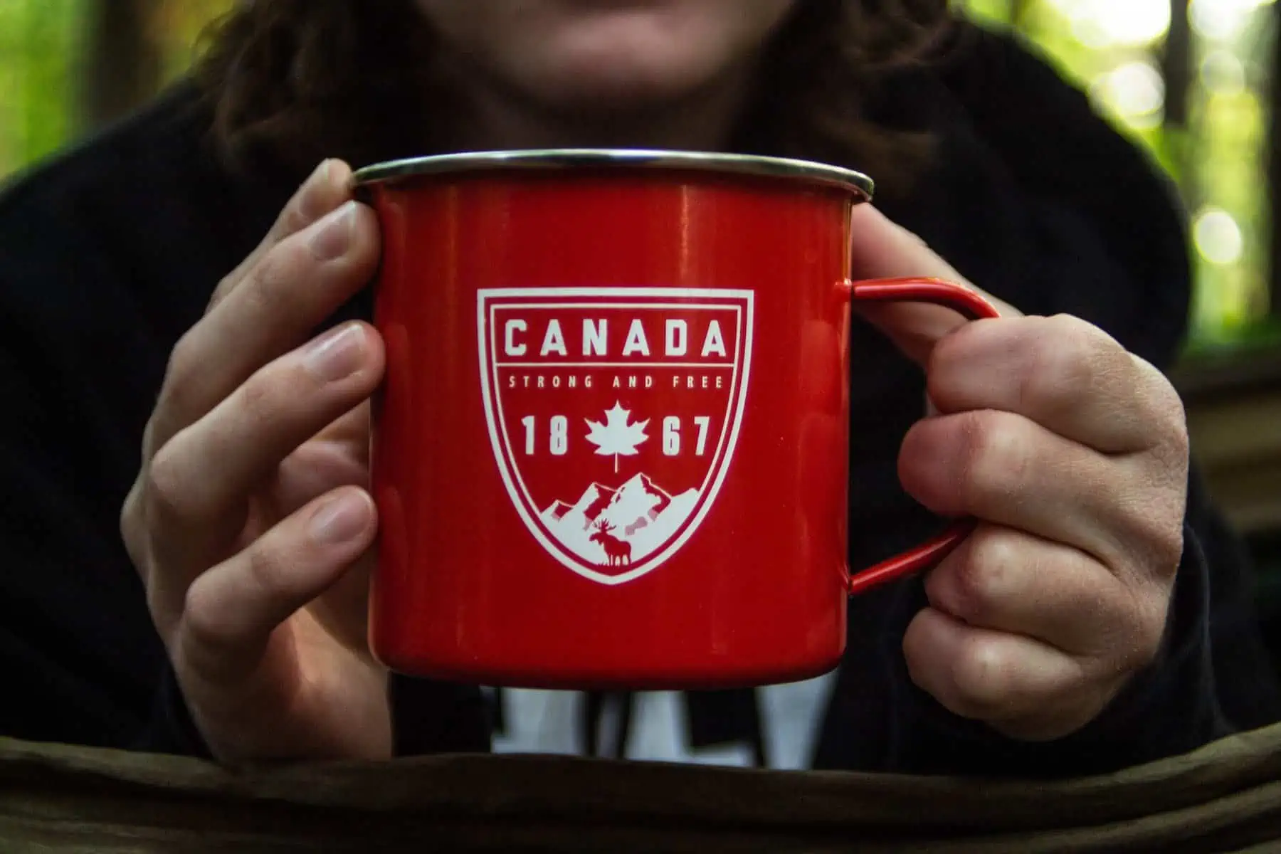Hands holding a red cup that says "Canada, Strong and Free, 1867"