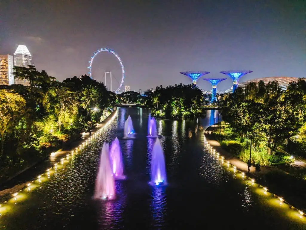 Waterfront in Singapore at night with fountains lit up; the ferris wheel and Supertree Grove are lit up in the background