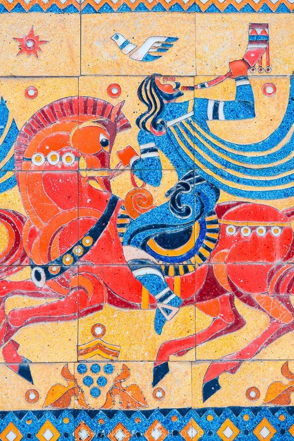 A man in a blue cloak blows a trumpet whilst riding a horse, as depicted in a Soviet-style mosaic on the Georgian Military Highway.