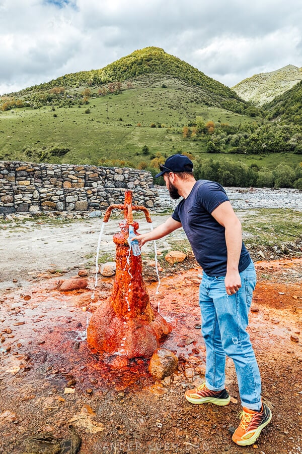 A man filling up a water bottle at a natural spring on the road side in Kazbegi, Georgia.