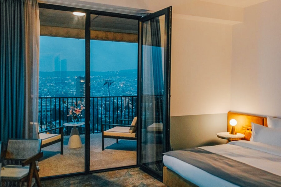 A modern boutique hotel room in Tbilisi, with a glass door and city views.