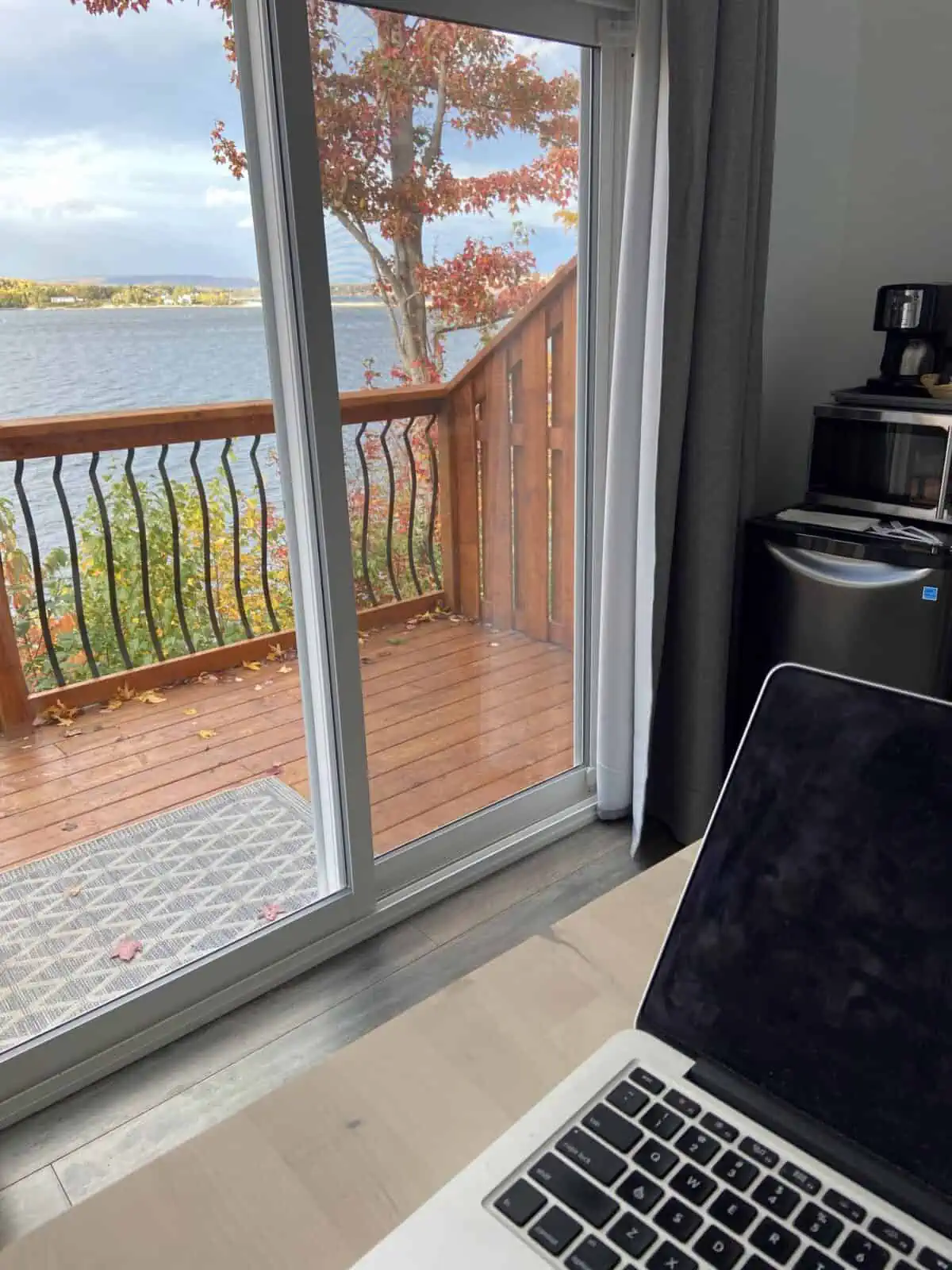 Laptop sitting on a desk with a view of fall foliage out the screen door behind it