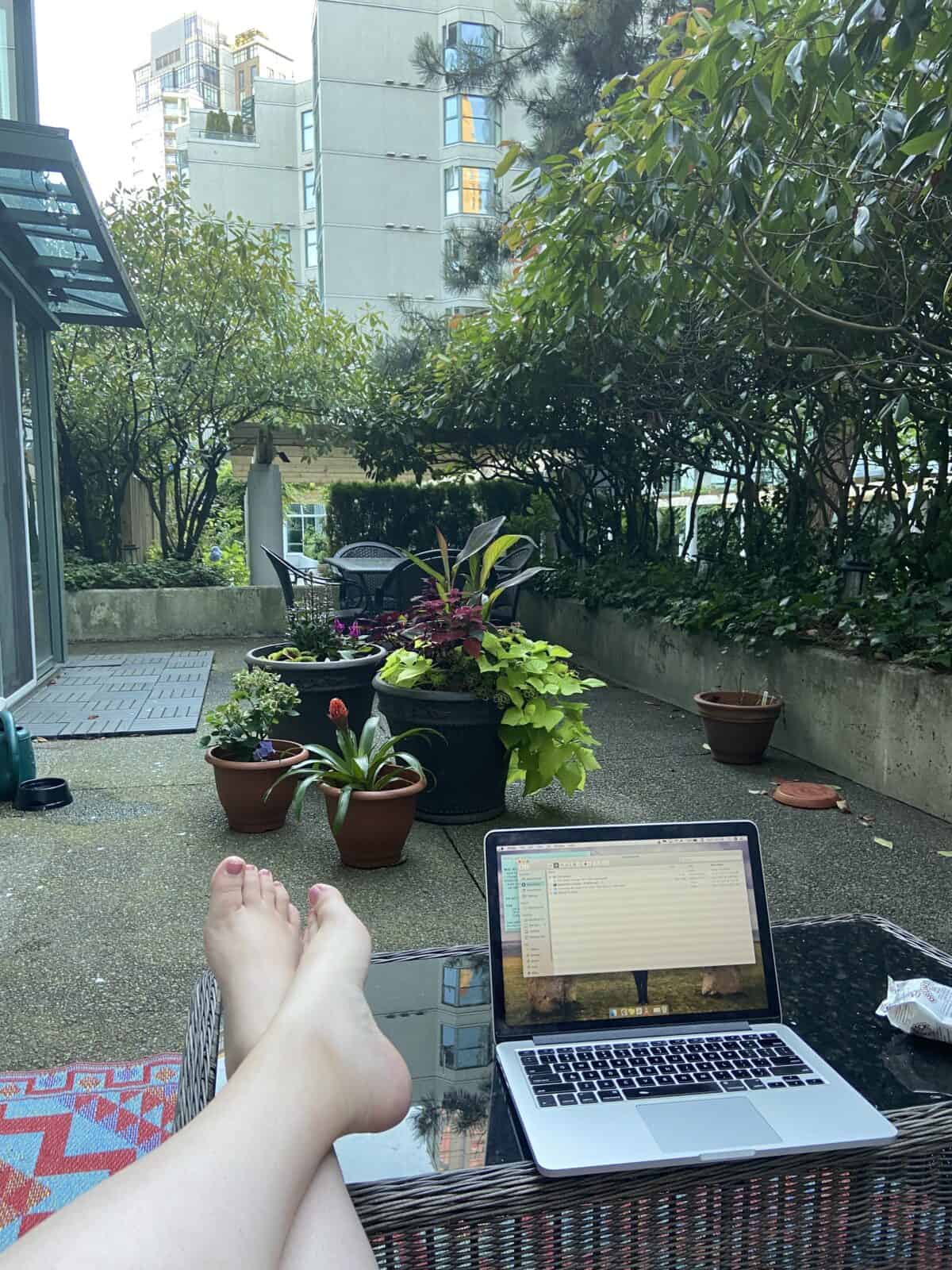 Working from the balcony with my legs crossed up on the coffee table, laptop in front of me and looking out at our plants and patio table