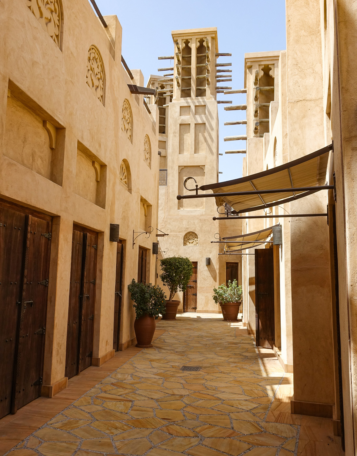 A narrow street through the souq lined with sand-colored buildings and a square tower in the background in Dubai.