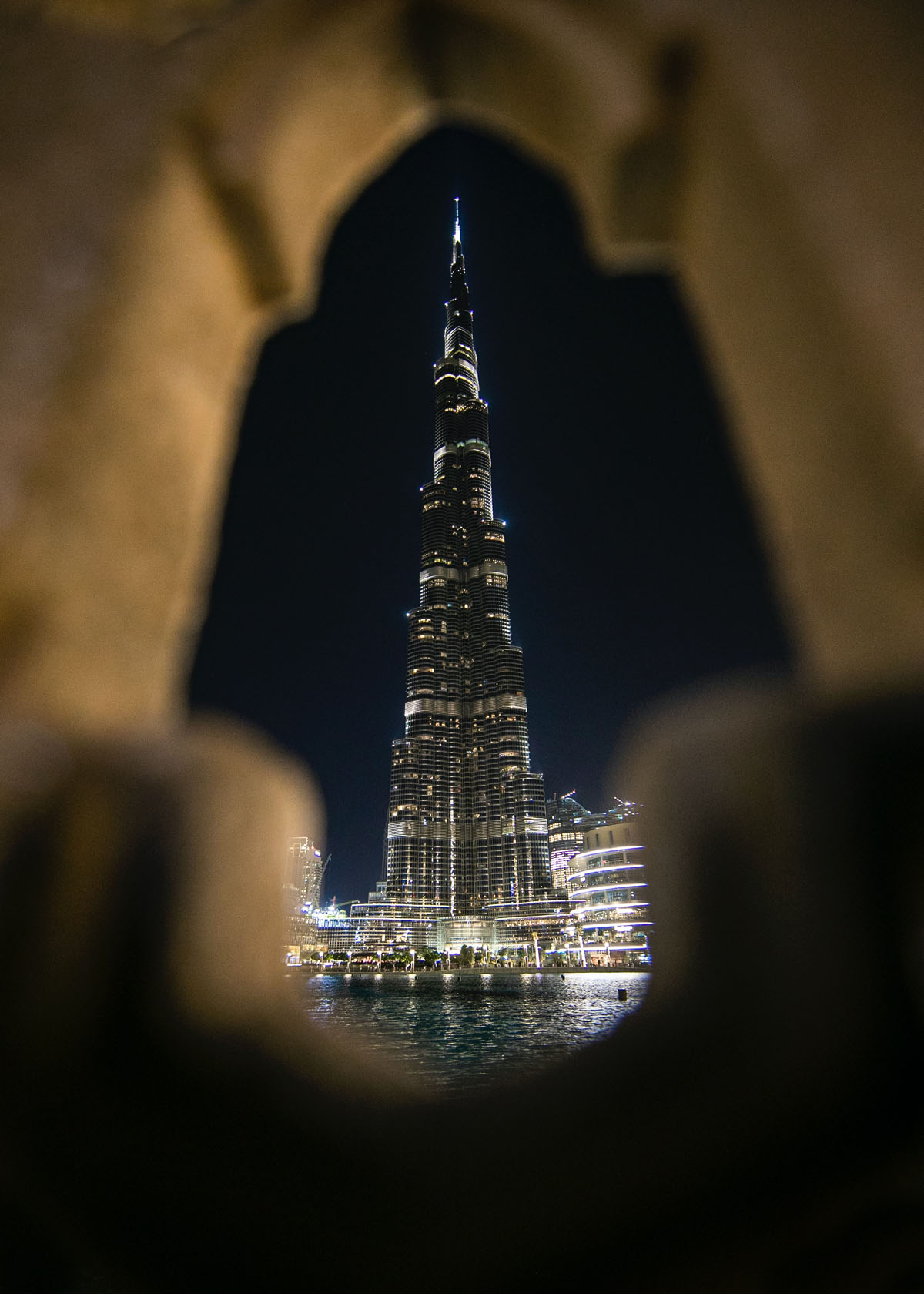 The enormous Burj Khalifa in Dubai rises up as seen through an arched gap in a gate.