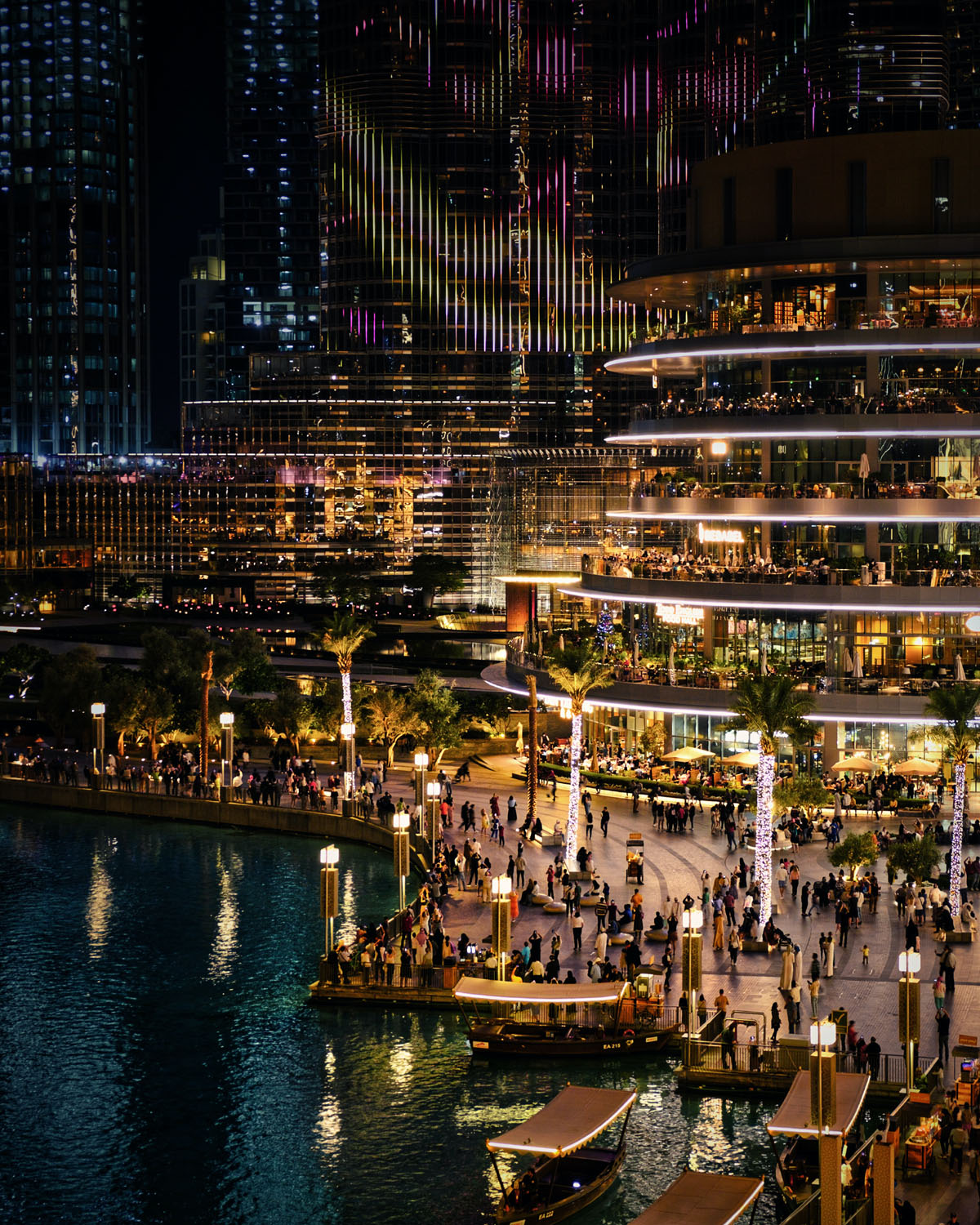 The glittering multi-story Dubai mall seen in the evening glowing with lights that are reflected in a nearby pool of water. 