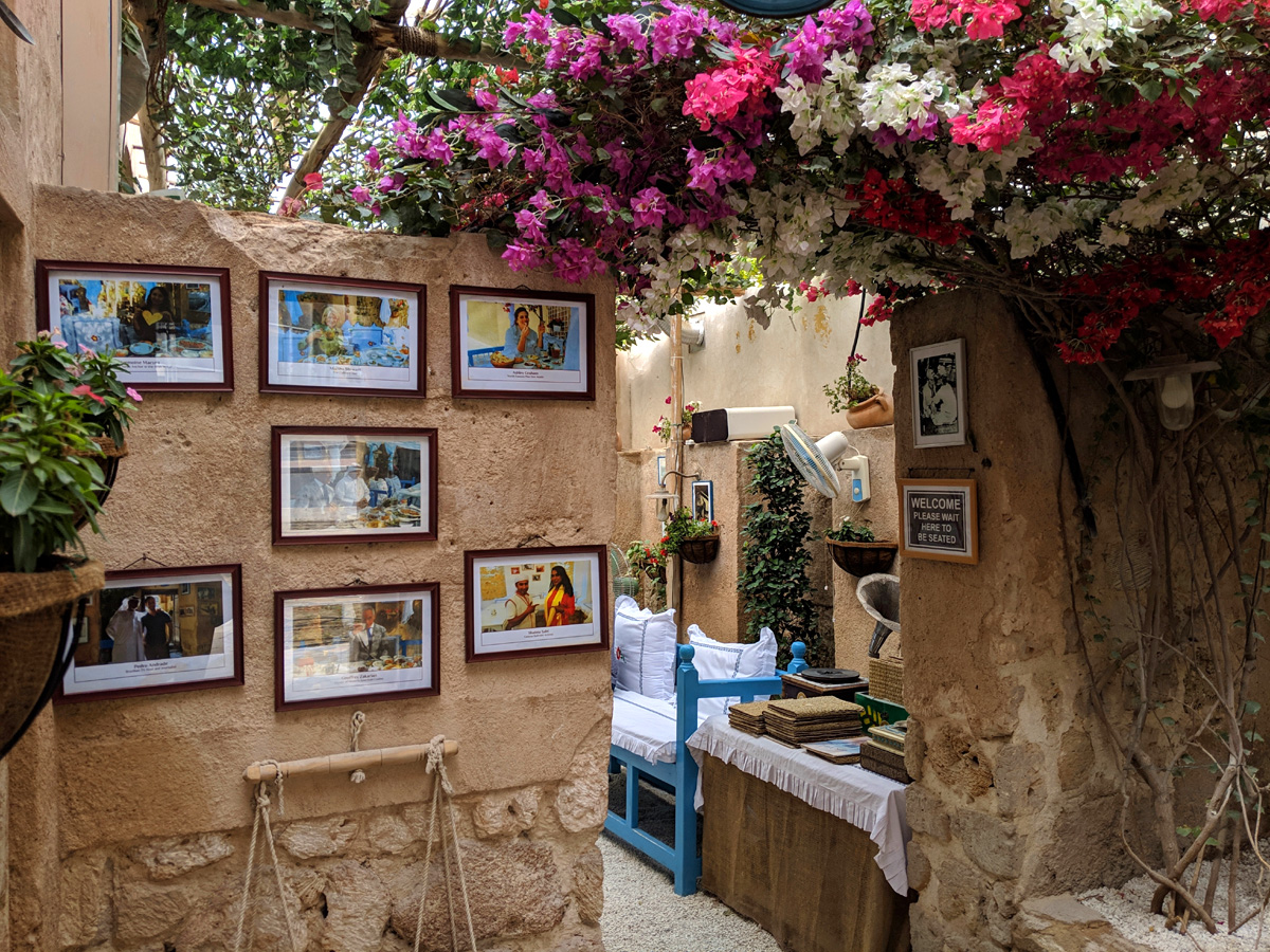 A coffee house in Dubai inside a small beige building surrounded by framed pictures on the wall and pink flowers. 