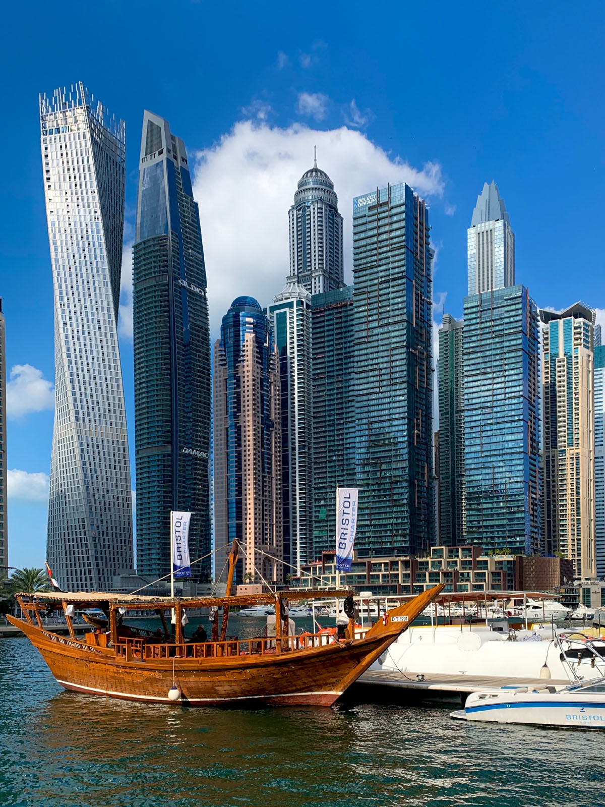 Skyscrapers line the waterfront in Dubai with an old traditional wooden boat in the foreground. 