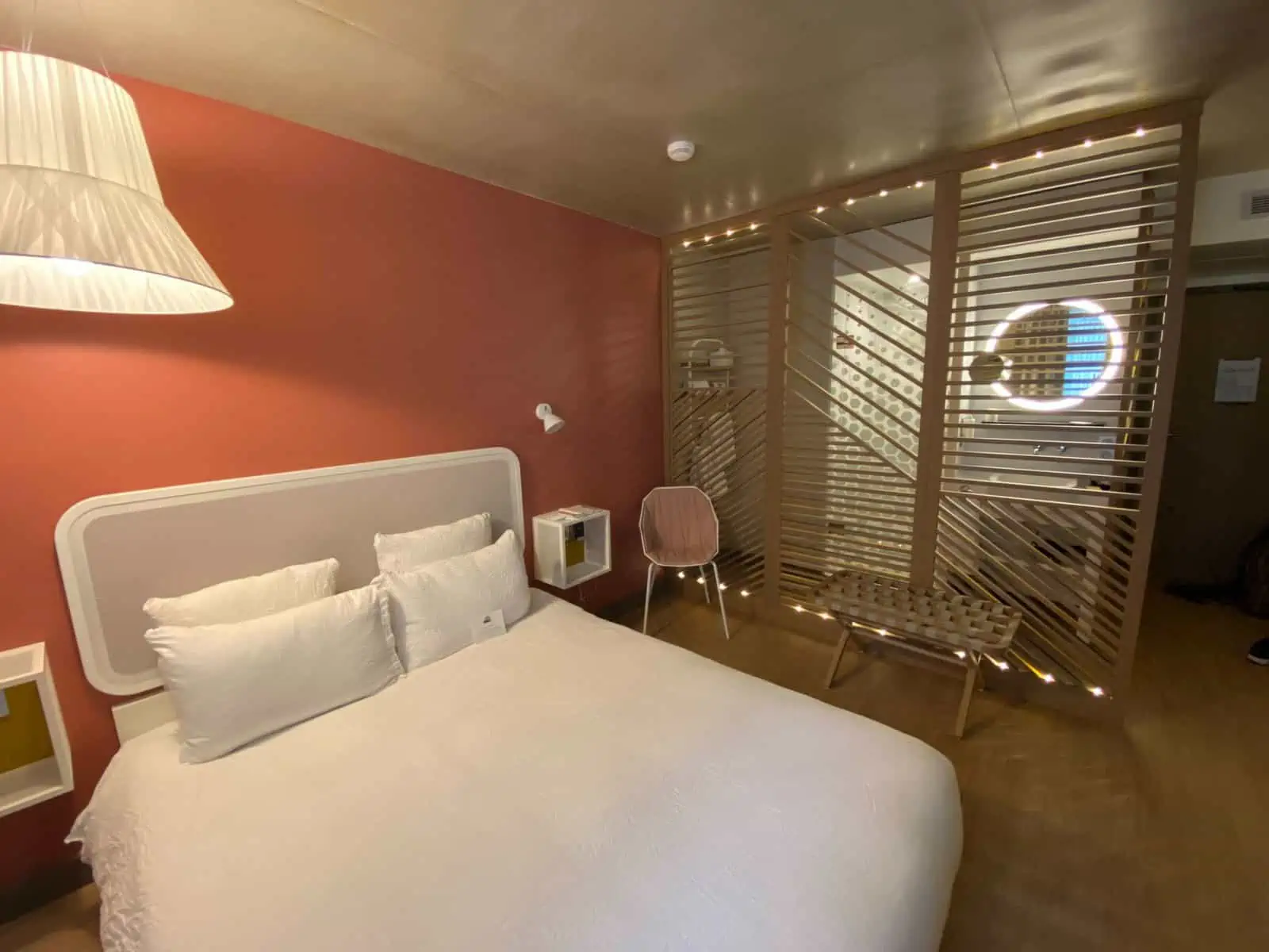 Room at OKKO Hotels in Paris, France featuring a large white bed, peach wall and wood slat decor