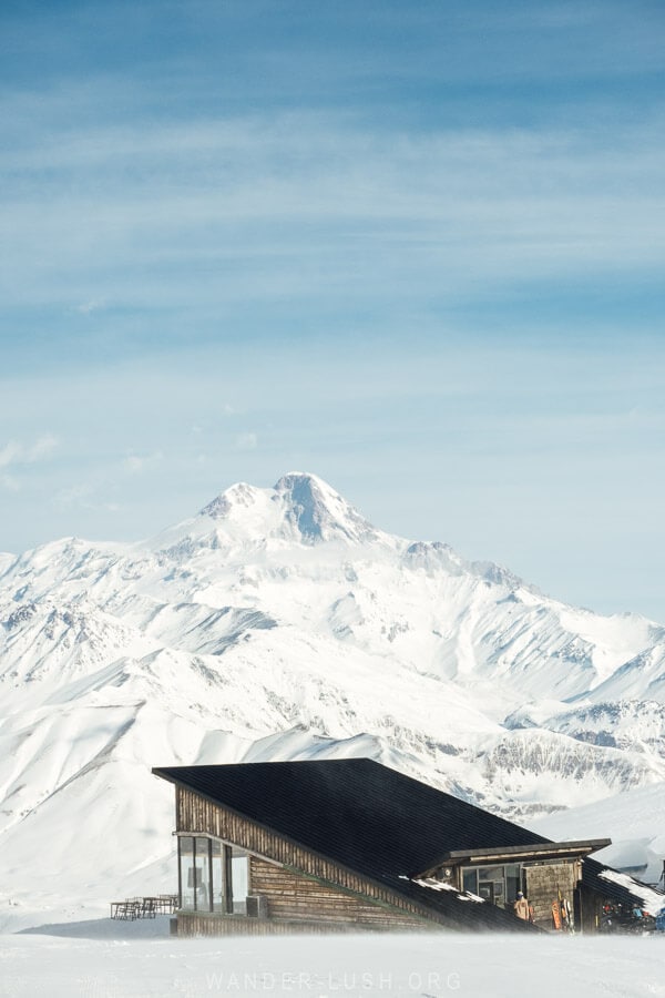 A mountain hut with a pitched roof in front of Mount Kazbek in Georgia.