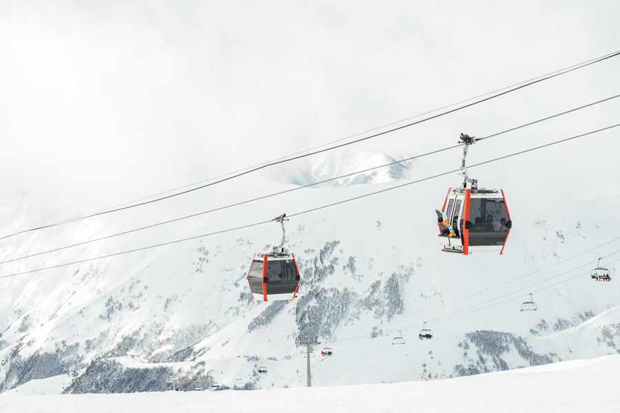 Two modern black and red gondolas moving along the Kobi Gudauri cable car line in the mountains of Georgia.