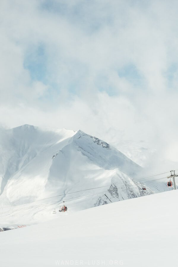 Cable cars dangling in front of tall snow covered mountains in Gudauri.