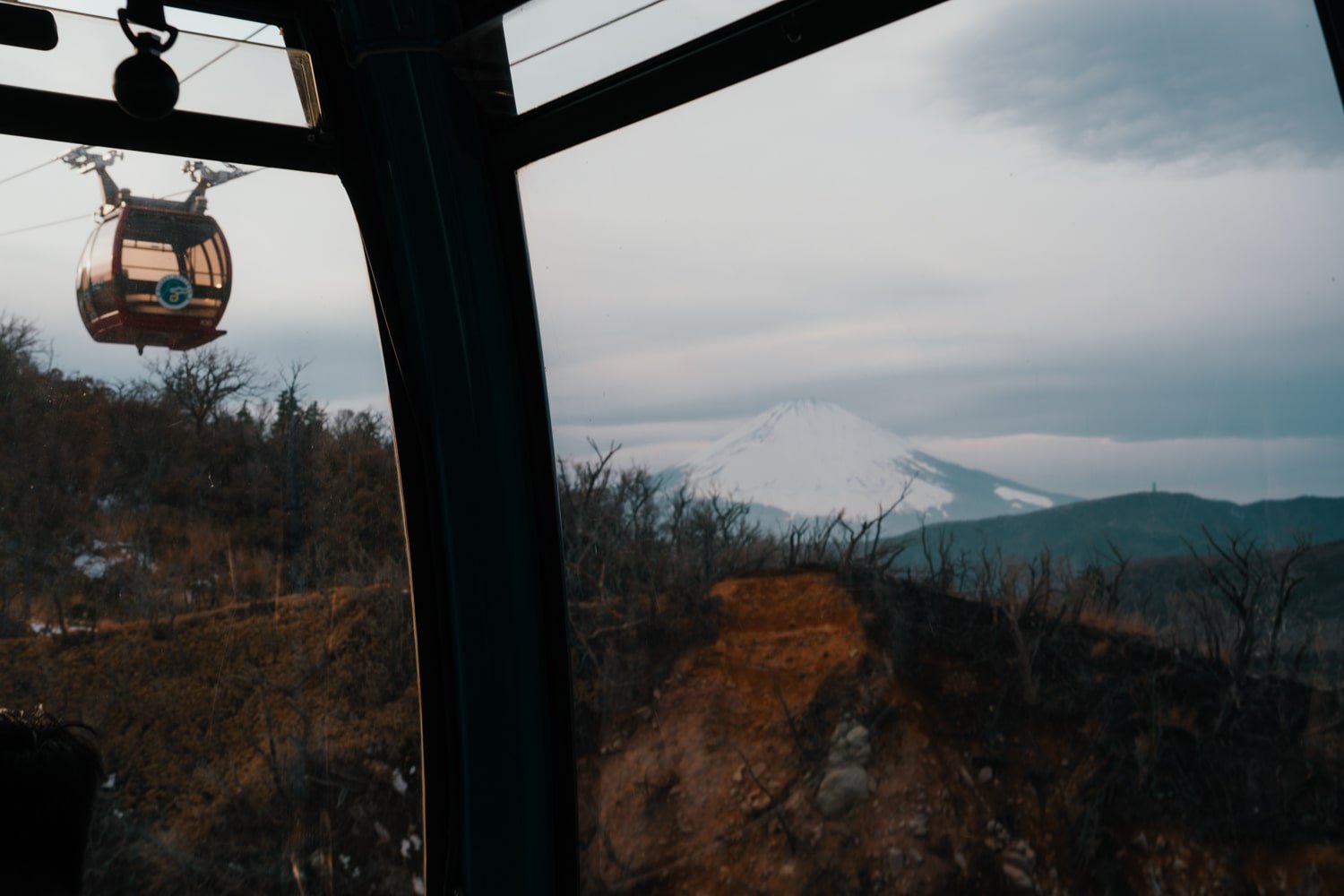 A view of an aerial tram car (Hakone Ropeway) over Owakudani sulphur fields with Mount Fuji in the background.