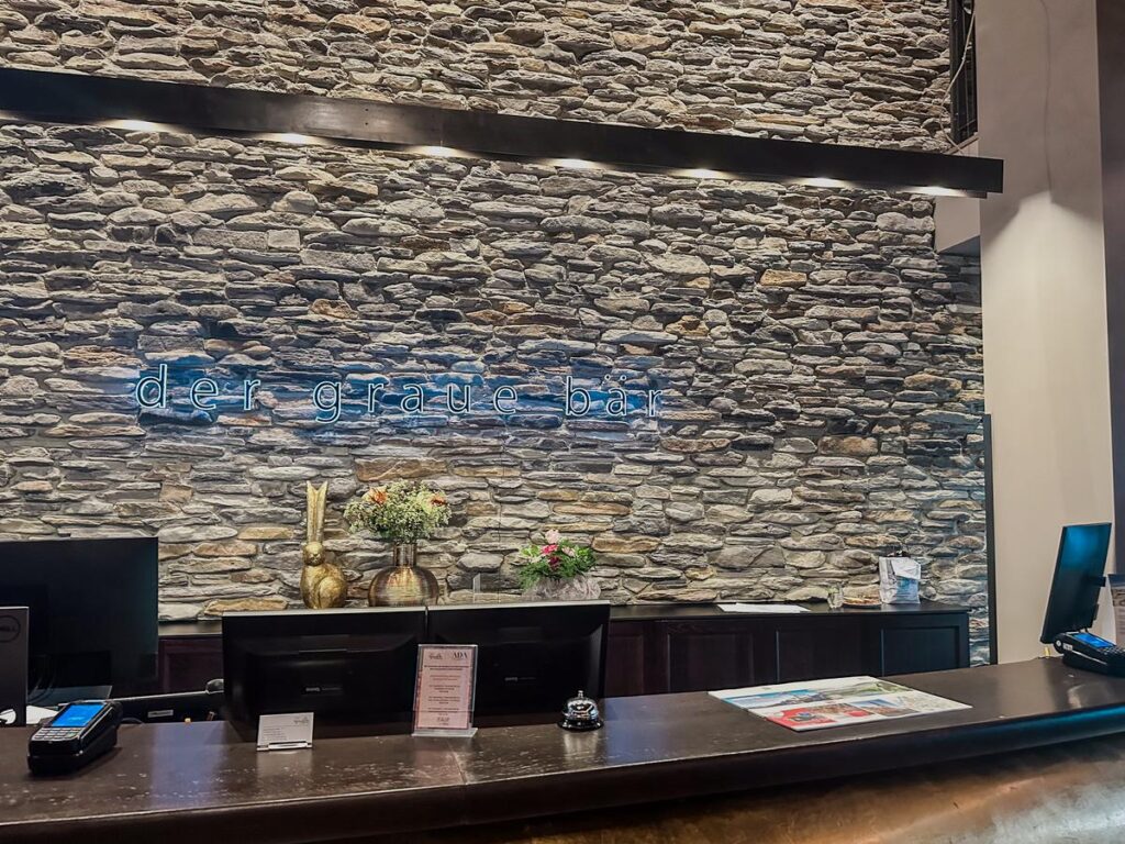 Elegant Hotel Grauer Bär lobby with rustic stone wall and modern reception area.