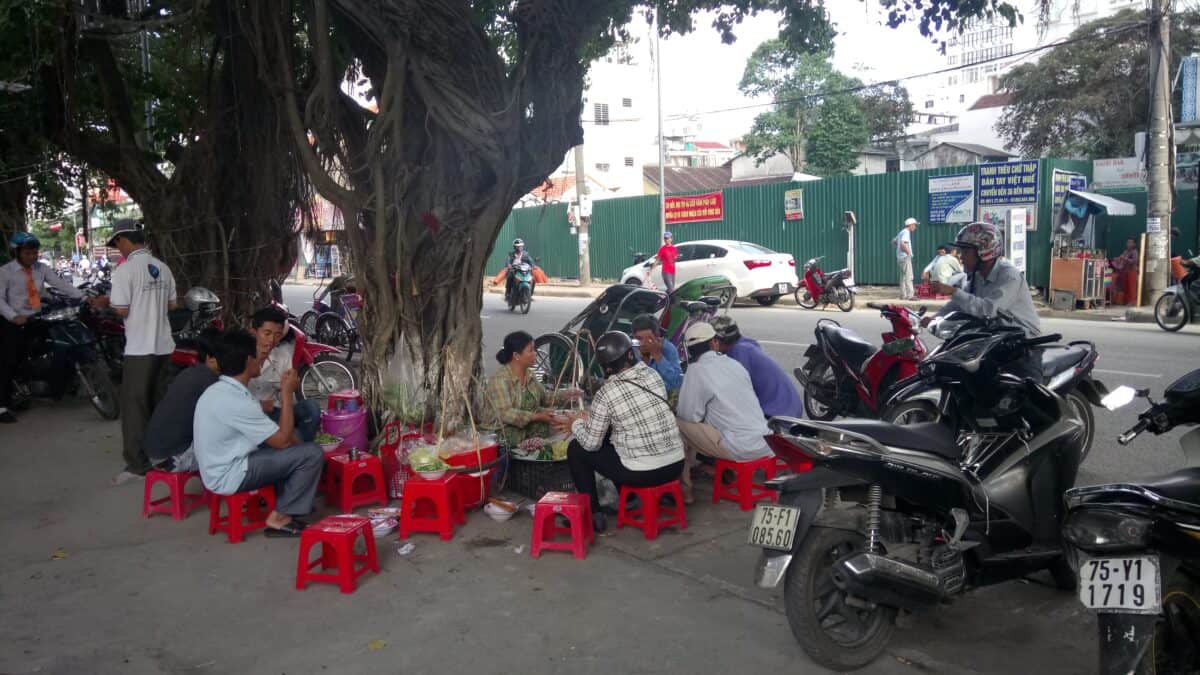 Street food stall in Hue, Vietnam with patrons sitting on red plastic stools 