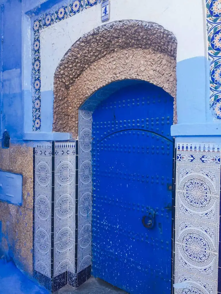 Blue door in Chefchaouen Morocco with ornate archway above it and columns next to it 