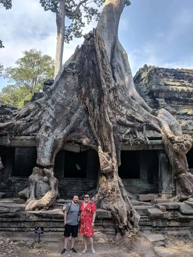 Riana and Colin in front of an overgrown tree and temple in the Angkor Wat temple complex in Cambodia