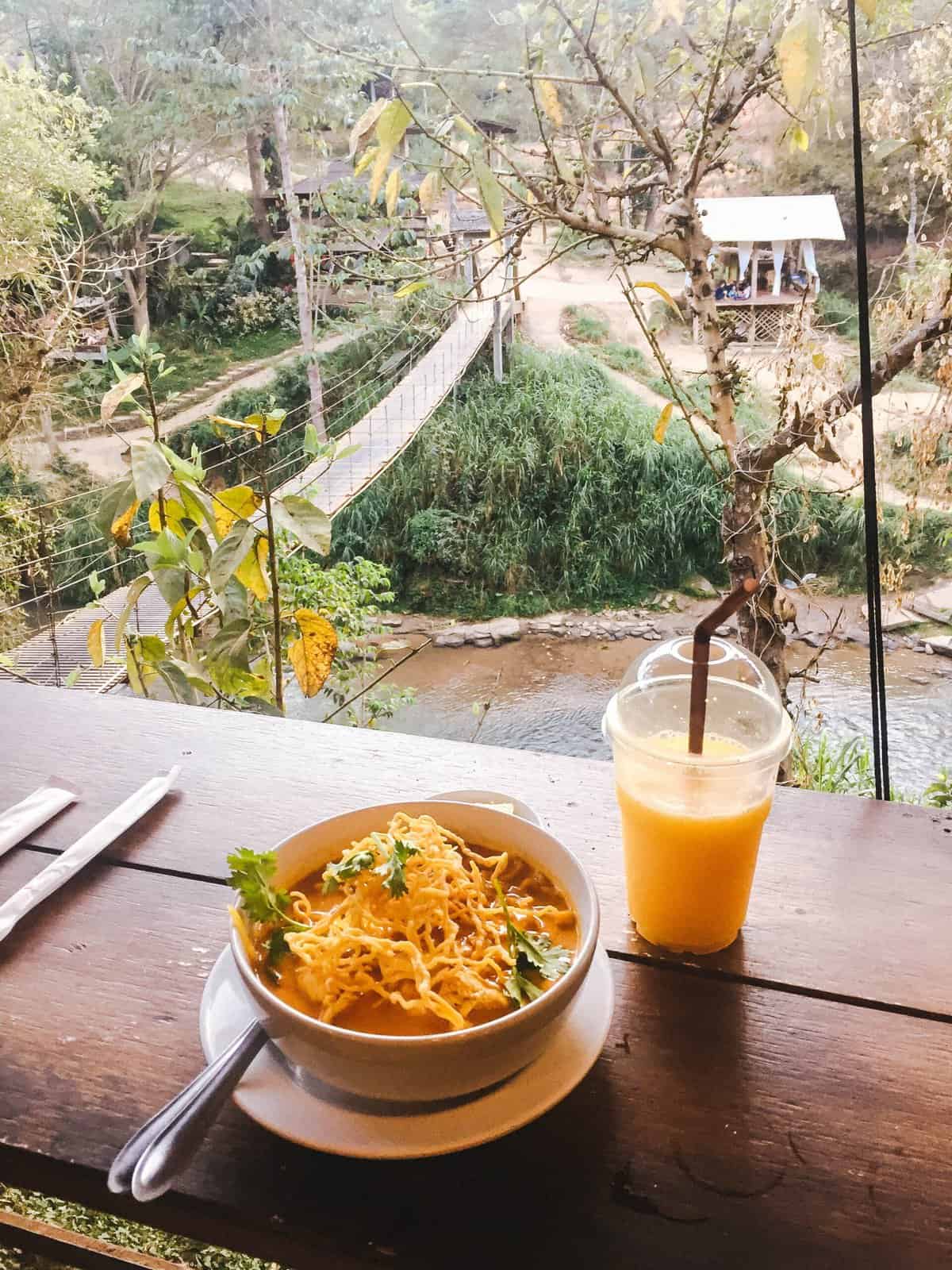 A bowl of Khao Soi and a mango shake with a view over Chai Lai Orchid, where you can visit elephants in Chiang Mai, Thailand