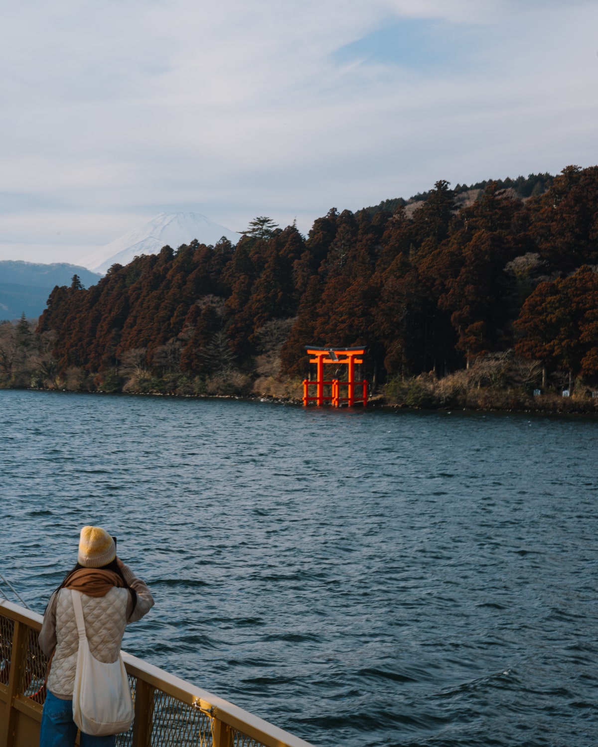 A woman on the Hakone cruise takes a photo of the red Hakone Shrine Torii gate rising out of the water at Lake Ashi in Hakone, Japan.