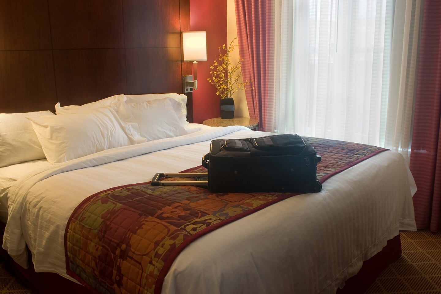 Hotel bed with throw across the foot and suitcase on top of it