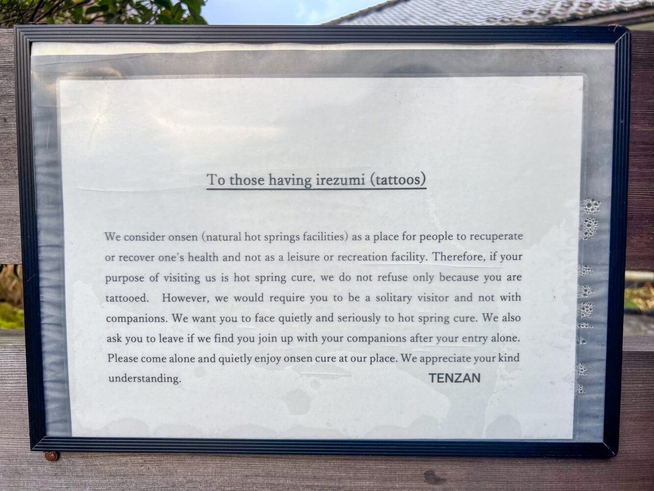 A white sign with black text explaining that the Tenzan Onsen in Hakone welcomes tattoos (irezumi).