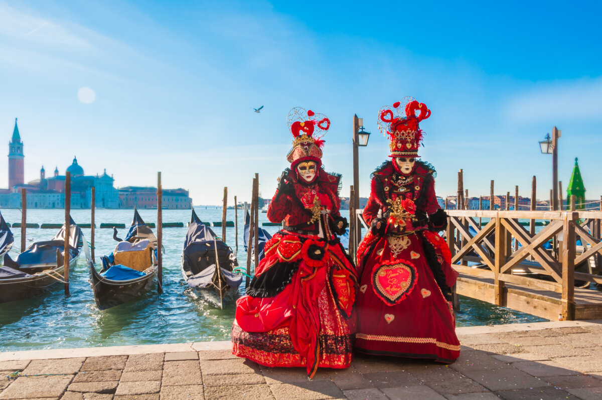 Couple wearing venitian carnival mask in front of gondolas in Grand Canal during Venice carnival in Italy