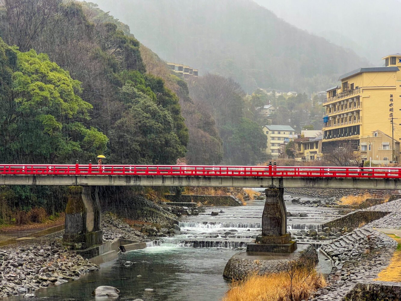 A rainy day in Hakone with a scene of a red pedestrian bridge over the Haya River in Hakone-Yumoto.