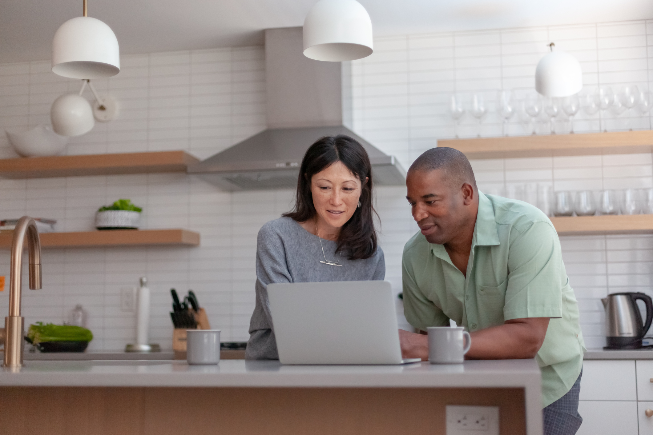 Two people staring at computer in kitchen. 