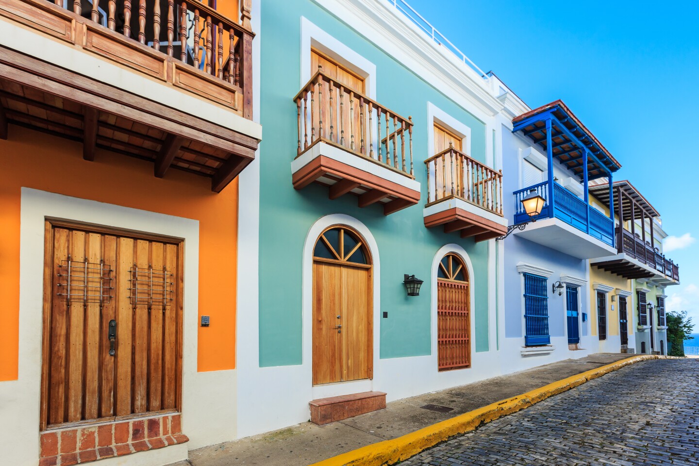 Row of orange, green, blue, and yellow homes, with second-story balconies, lining a cobblestone street in Old San Juan, Puerto Rico